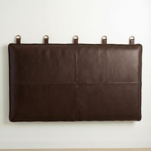 May include: A rectangular, dark brown leather headboard with four stitched panels. The headboard has four leather straps with metal rings at the top for hanging. The headboard is approximately 48 inches wide and 24 inches tall.