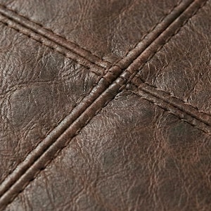 May include: Close-up of dark brown leather with visible texture and stitching. The stitching forms a cross pattern, adding detail to the material. The leather appears to be aged, with variations in color.