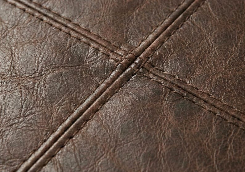 May include: Close-up of dark brown leather with visible texture and stitching. The stitching forms a cross pattern, adding detail to the material. The leather appears to be aged, with variations in color.