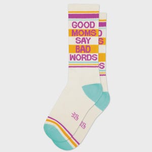 May include: A pair of off-white socks with the text "GOOD MOMS SAY BAD WORDS" in purple, orange, and light blue. The socks have light blue heels and toes, with purple and orange stripes at the top and bottom.