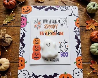 May include: A white ghost-shaped squishy toy centered on a rectangular card featuring Halloween graphics, including pumpkins, bats, and spiderwebs. The card text reads: Have a squishy spooky Halloween from Maddison, with a small ghost graphic and the word Boo.