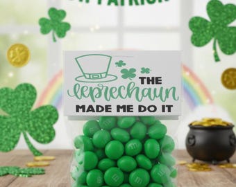 May include: A clear cellophane bag filled with green candies, with the text "The leprechaun made me do it." The bag is on a wooden surface, with gold coins and shamrock decorations. A banner reads "Happy St. Patrick's Day!"