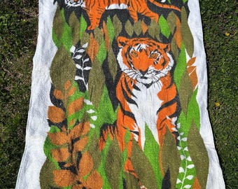 May include: White rectangular towel with a jungle scene featuring two orange tigers amongst green and brown foliage. The towel has a fringed edge. The design is reminiscent of vintage textile art, with a retro aesthetic.