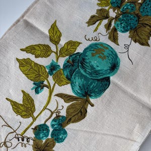 May include: A light beige linen-textured fabric featuring a printed botanical pattern of teal-coloured berries and fruits with olive green leaves and thin brown stems. The design includes small curling tendrils and clusters of round fruit.