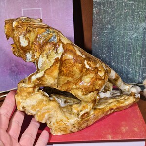 May include: A detailed sculpture of a roaring tiger, crafted from a stone with a mix of brown, tan, and white hues. The tiger is posed on a textured base, showcasing intricate details and a naturalistic style. The sculpture is a decorative item.