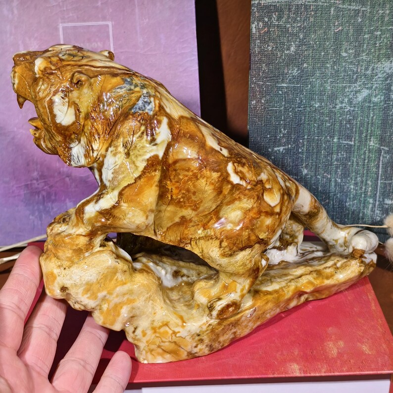 May include: A detailed sculpture of a roaring tiger, crafted from a stone with a mix of brown, tan, and white hues. The tiger is posed on a textured base, showcasing intricate details and a naturalistic style. The sculpture is a decorative item.