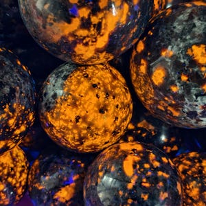 May include: Close-up of several spherical objects with a speckled pattern. The spheres have a dark base colour with bright orange and black spots. Some spheres have hints of blue. The spheres are smooth and appear to be made of stone or a similar material.