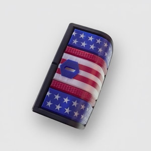Op de afbeelding: Een rechthoekige zwarte kunststof schakelaarafdekking met een patriottisch ontwerp, voorzien van blauwe secties met witte sterren aan de boven- en onderkant, en een middengedeelte met rode en witte horizontale strepen en een klein blauw zeshoekig embleem.