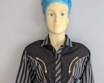 May include: Black and white striped shirt with a black yoke and gold arrow embroidery. The shirt has long sleeves and a button-down front. The shirt is displayed on a mannequin with blue hair.