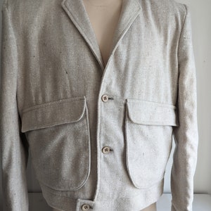 May include: A light beige linen blazer with a slightly cropped fit. The blazer has a notched collar, four button closures, and two large patch pockets.