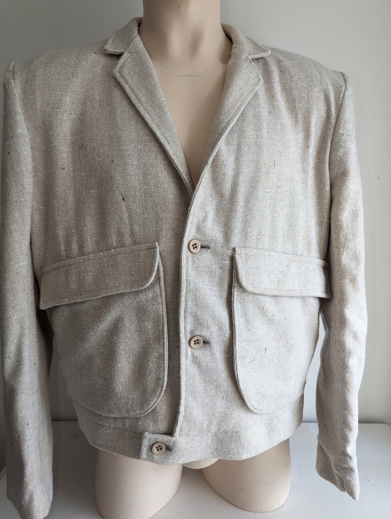 May include: A light beige linen blazer with a slightly cropped fit. The blazer has a notched collar, four button closures, and two large patch pockets.