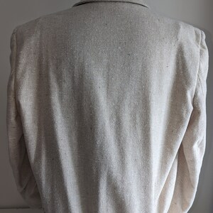 May include: A beige linen blazer with a slightly textured fabric. The blazer has a classic style with a notched collar and long sleeves.