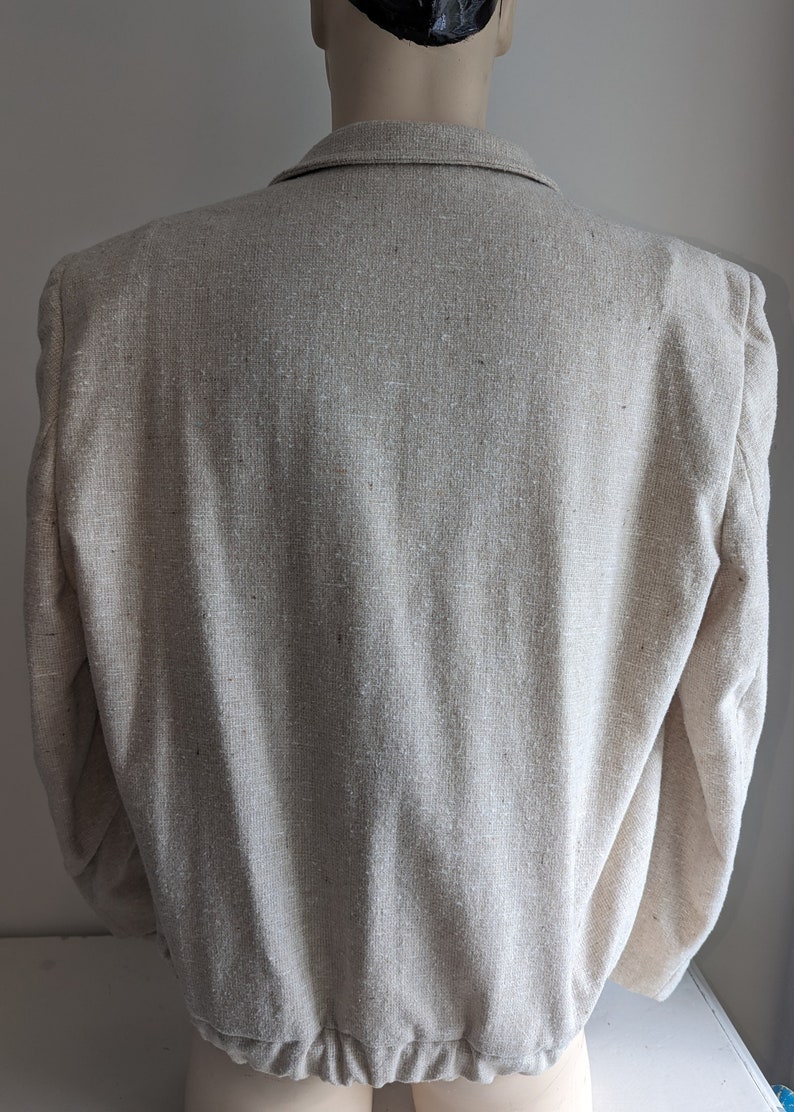 May include: A beige linen blazer with a slightly textured fabric. The blazer has a classic style with a notched collar and long sleeves.