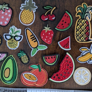 Könnte beinhalten: Eine Sammlung bunter, gestickter Flicken mit Früchten wie Erdbeeren, Ananas, Wassermelonen, Kirschen, Orangen, Bananen und einer Zitrone. Die Aufnäher in verschiedenen Größen und Designs eignen sich perfekt zum Dekorieren von Kleidung oder Accessoires.