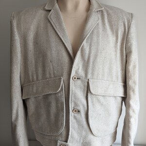 May include: A light beige linen blazer with a button closure and two large patch pockets. The blazer has a relaxed fit and a cropped length.