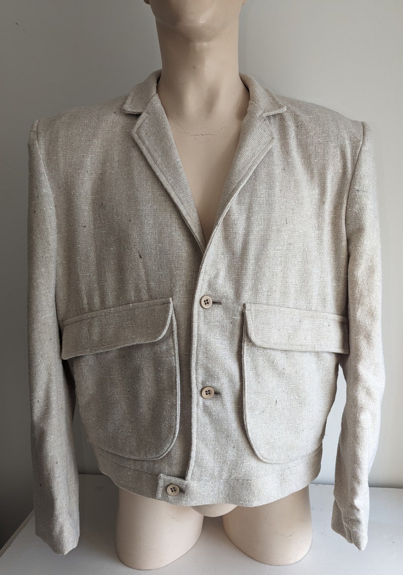May include: A light beige linen blazer with a button closure and two large patch pockets. The blazer has a relaxed fit and a cropped length.