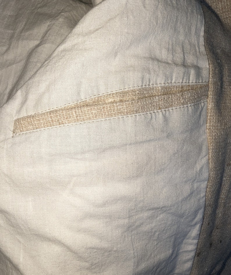 May include: Close-up of the inside of a garment, showing a beige linen fabric with a seam detail. The seam is made of a woven beige fabric and is stitched with a straight stitch.