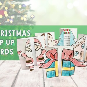 May include: Christmas pop-up cards with festive designs including Santa Claus, a gingerbread man, a Christmas tree, a house, and wrapped gifts. The cards are white with colourful illustrations. The text "Merry Christmas!" is visible. A Christmas tree is in the background.