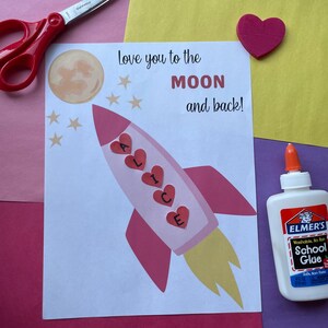 May include: A handmade card with a pink rocket ship design, the name "ALICE" in hearts, and the text "Love you to the MOON and back!". Includes scissors, glue, and a pink heart on a colorful background.