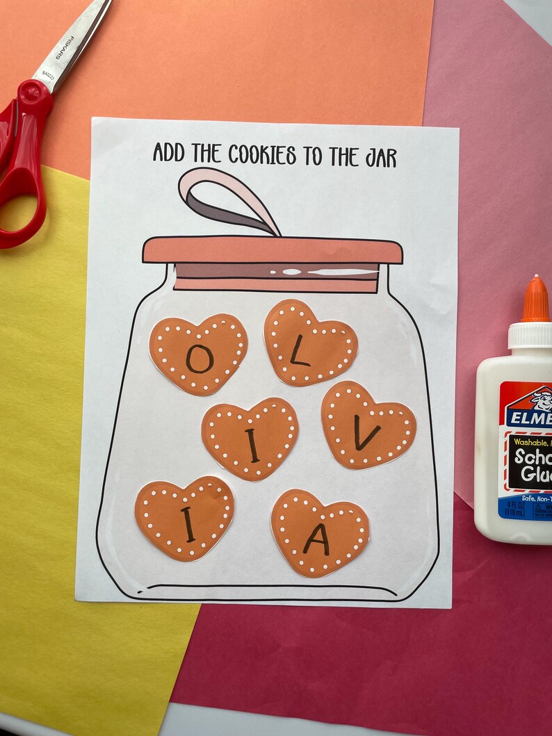 May include: A craft project featuring a drawing of a jar with heart-shaped cookies inside, spelling out the name "Olivia". The text "ADD THE COOKIES TO THE JAR" is above the jar. Scissors and glue are visible on the colorful background.