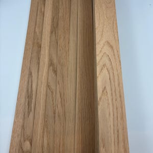 Könnte beinhalten: Eine Sammlung unfertiger Eichenholzbretter in hellem Farbton. Die Bretter sind vertikal angeordnet und zeigen die natürliche Holzmaserung und -struktur. Das Holz scheint für ein Holzbearbeitungsprojekt bereit zu sein.