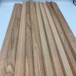 Könnte beinhalten: Eine Ansammlung unfertiger Holzbretter, fächerförmig angeordnet. Die Bretter sind rechteckig, mit natürlicher Holzmaserung und hellbrauner Farbe. Das Holz scheint neu zu sein und für ein Holzbearbeitungsprojekt bereit zu sein.