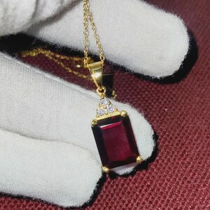 May include: A gold necklace featuring a rectangular, deep red gemstone pendant. The pendant is adorned with small, clear stones and hangs from a fine chain. The necklace is shown against a white background.