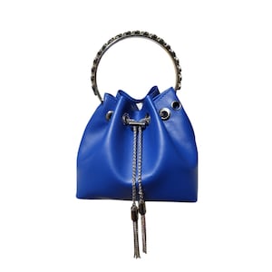 May include: A vibrant cobalt blue bucket bag with a silver chain handle and drawstring closure. The bag has silver grommets and a silver chain tassel detail. The bag is made of a smooth, leather-like material.