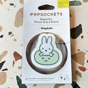 May include: A white PopSockets magnetic phone grip and stand in its retail packaging. The product features a graphic of a white rabbit character sitting on a light green circular base. The packaging includes the text PopSockets, Magnetic Phone Grip & Stand, and MagSafe, along with a small diagram showing the product attached to a phone.