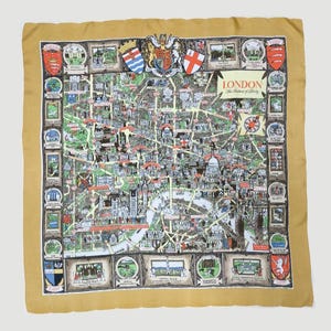 May include: Mustard-colored square scarf featuring a detailed map of London, England. The map is surrounded by framed illustrations of landmarks and city emblems. The text "London The Heart of Liberty" is visible.