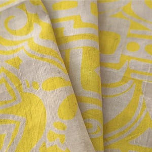 May include: A piece of fabric featuring a bright yellow and off-white abstract pattern. The textile displays a repeating graphic design with curved lines and geometric shapes printed on a textured surface with visible horizontal and vertical threads.