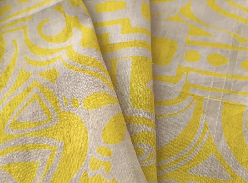 May include: A piece of fabric featuring a bright yellow and off-white abstract pattern. The textile displays a repeating graphic design with curved lines and geometric shapes printed on a textured surface with visible horizontal and vertical threads.