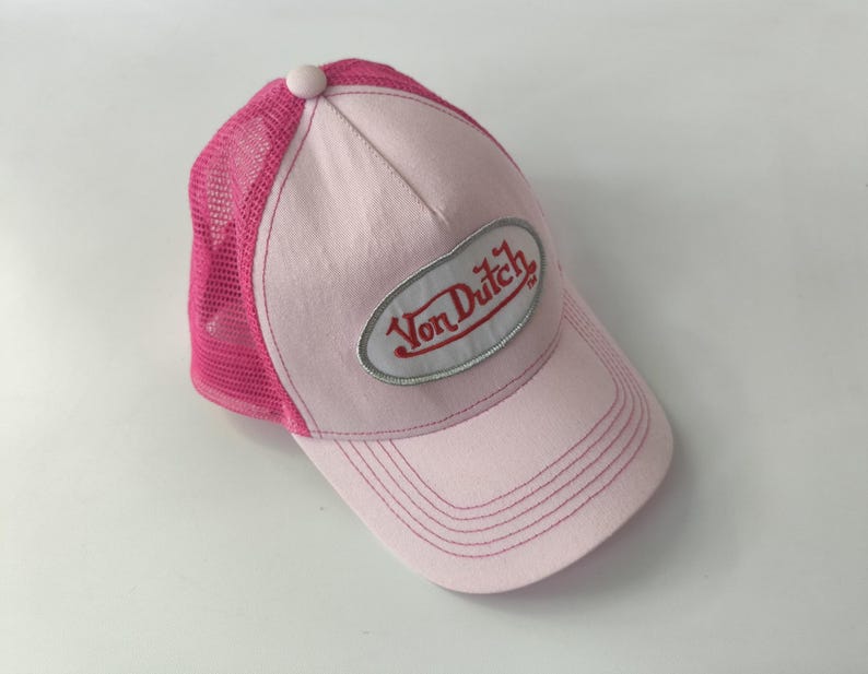 May include: A light pink trucker hat featuring a mesh back in a vibrant hot pink color. The front panel is solid light pink with a central oval patch containing the red text Von Dutch. The hat includes a curved brim with matching pink stitching.