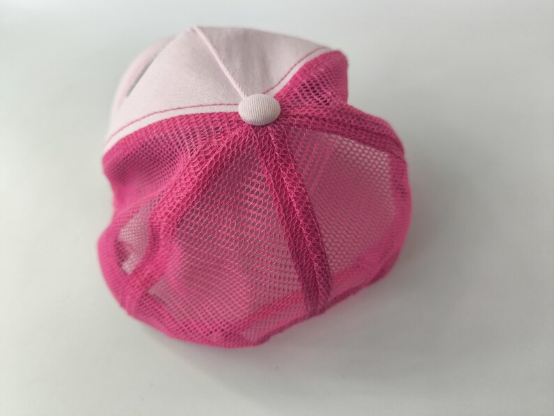 May include: A baseball cap featuring a light pink front panel and a vibrant hot pink mesh back. The cap includes a matching fabric-covered button at the center top where the panels meet, showcasing a structured design with breathable mesh sections.