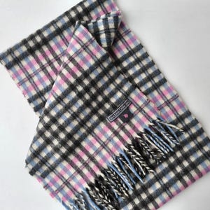 Peut inclure: Écharpe à carreaux noirs, blancs, bleu clair et roses. L'écharpe a une bordure à franges et une étiquette indiquant "Sinclair Duncan". L'écharpe est pliée sur elle-même.