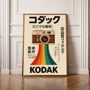 May include: A framed vintage Kodak poster. The poster features a brown and tan camera with a rainbow design. Japanese text and the Kodak logo are also visible. The frame is made of wood.