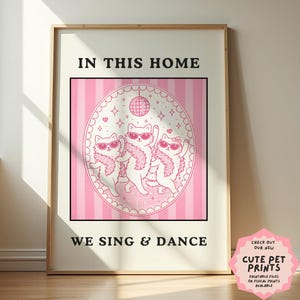 Può includere: Una stampa incorniciata con la scritta "IN THIS HOME WE SING & DANCE". L'opera presenta tre gatti bianchi con occhiali da sole e boa rosa, che ballano in una cornice ovale rosa. Una palla da discoteca e cuori sono anche nella cornice. Un adesivo rosa nell'angolo dice "CUTE PET PRINTS".