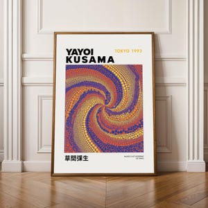 Può includere: Una stampa artistica incorniciata con un motivo a spirale di punti arancioni, gialli e viola. La stampa include il testo "YAYOI KUSAMA TOKYO 1993" e caratteri giapponesi. L'opera d'arte è esposta su un pavimento in legno.