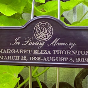 May include: A dark bronze memorial plaque with the words "In Loving Memory" and the name "MARGARET ELIZA THORNTON" and dates "MARCH 12, 1932-AUGUST 8, 2019". The plaque has a decorative emblem at the top.