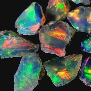 May include: A selection of rough opal gemstones, showcasing a play of colour. The opals exhibit a range of hues, including green, blue, orange, and yellow, set against a dark backdrop. The stones have a natural, unpolished appearance.
