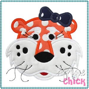 May include: Orange and white polka dot tiger face with a navy blue bow. The tiger has white fur around the nose and mouth with black whiskers.