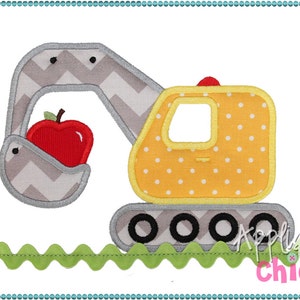 May include: A yellow toy excavator with a gray arm holding a red apple. The excavator has black wheels and a yellow cab with white polka dots. The excavator is on a green grass background.
