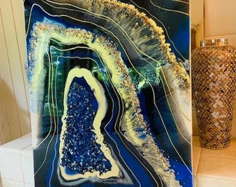 May include: Abstract resin art painting with blue, yellow, and gold colors. The painting features a swirling, agate-like design with gold glitter accents.