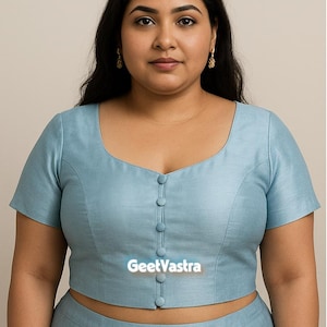 Puede incluir: Top corto azul claro con cuello cuadrado y mangas cortas. La parte superior tiene una fila de botones en el centro y el texto "GeetVastra" en la parte inferior. La modelo lleva una falda a juego.