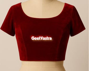 May include: A short-sleeved, claret velvet top with a scoop neckline. The garment is displayed on a mannequin. The text "GeetVastra" is displayed on the front of the top.