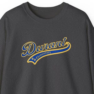 May include: A dark gray sweatshirt with the word "Durant" in a script font, outlined in gold and blue. Below the word "Durant" is the word "Elementary" in a smaller font. The sweatshirt has a crew neck and long sleeves.