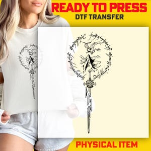 A woman wearing a white t-shirt with a graphic design featuring a stylized sword and a circular emblem.
