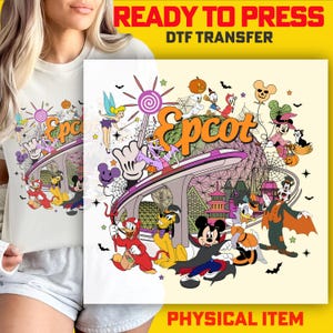 May include: White t-shirt featuring a colorful Halloween-themed graphic. The design includes the word "Epcot" in orange, various Disney characters in costumes, and Halloween elements like bats and pumpkins. The words "READY TO PRESS DTF TRANSFER" and "PHYSICAL ITEM" are also visible.