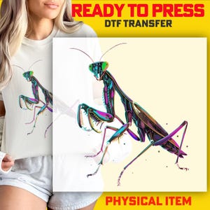 May include: A white t-shirt featuring a colorful graphic of a praying mantis. The insect design has vibrant hues of green, purple, and blue. The words "READY TO PRESS DTF TRANSFER" and "PHYSICAL ITEM" are displayed in the image.