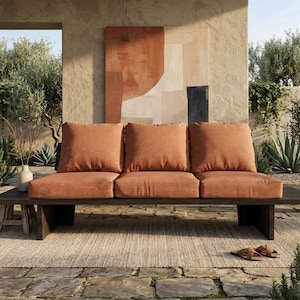 Może przedstawiać: Drewniana sofa ogrodowa z trzema pomarańczowymi poduszkami. Sofa stoi na kamiennym patio, z neutralnym dywanem i abstrakcyjnym dziełem sztuki w tle. Wymiary sofy to około 200 cm długości.